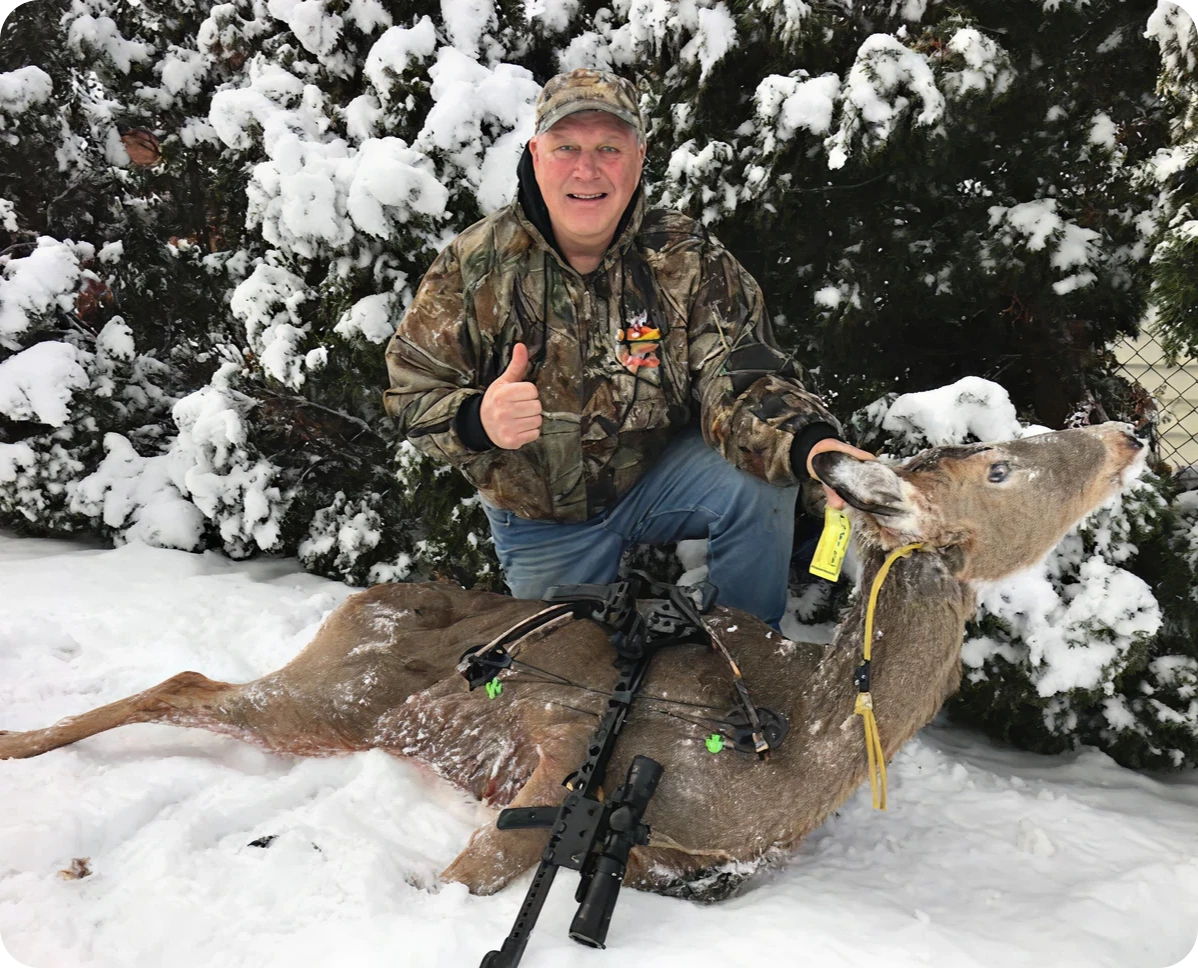 Camouflage-clad hunter beside downed deer